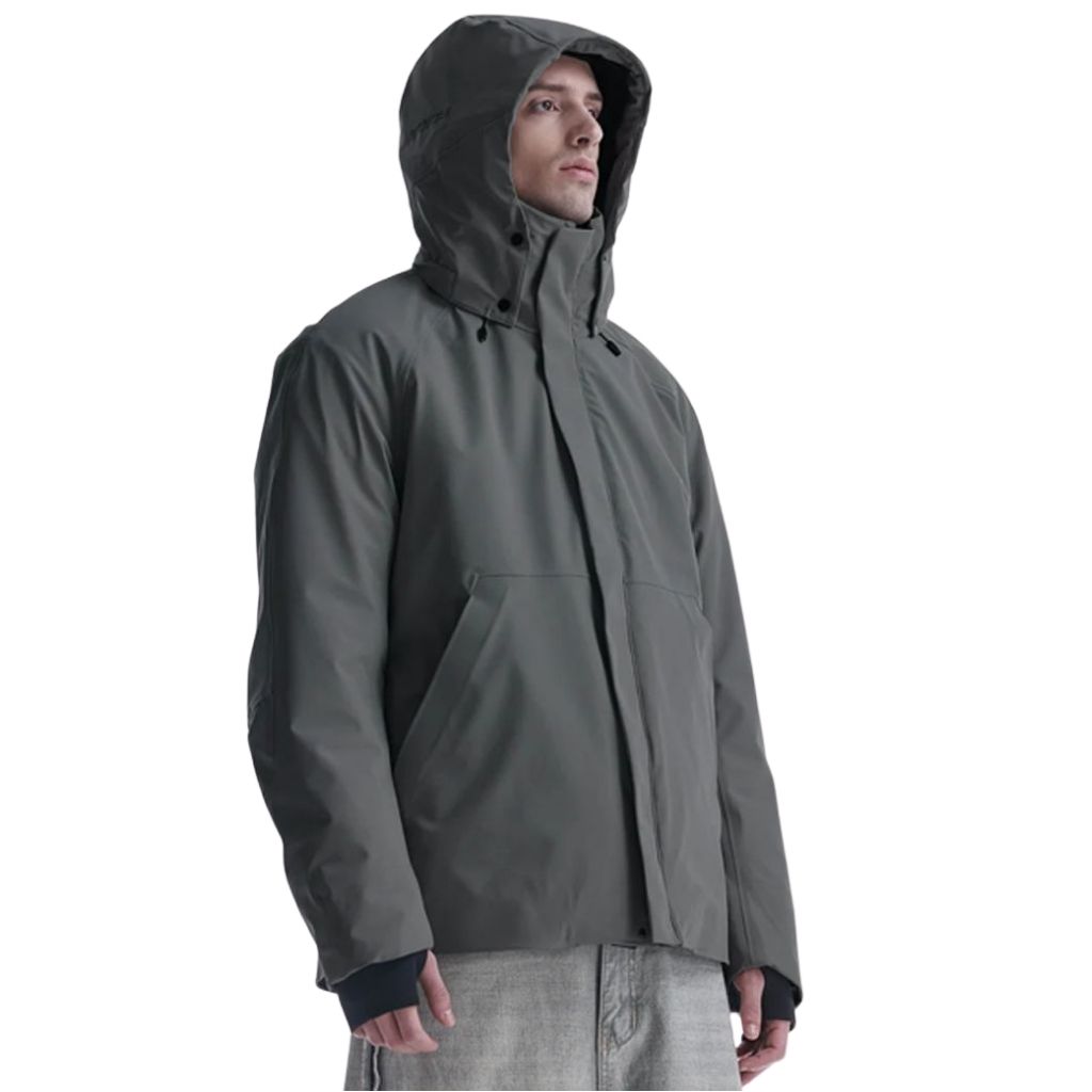 A man wearing a dark gray storm jacket with a hood, standing in a three-quarter profile. The jacket features a high collar, front zipper, and large front pockets, with ribbed cuffs peeking out from beneath.