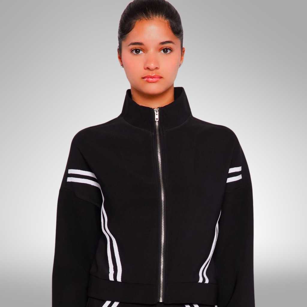 A young woman wearing a black zip-up jacket with white racing stripe accents on the sleeves and sides, standing against a neutral gray background.