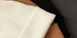Sustainable Cashmere Wool Fabric for Luxury Wear Sustainable Cashmere Wool Fabric A close-up of folded knitted hats stacked in a layered arrangement. The top hat is off-white with ribbed texture, followed by tan, black, and gray tones in the stack.