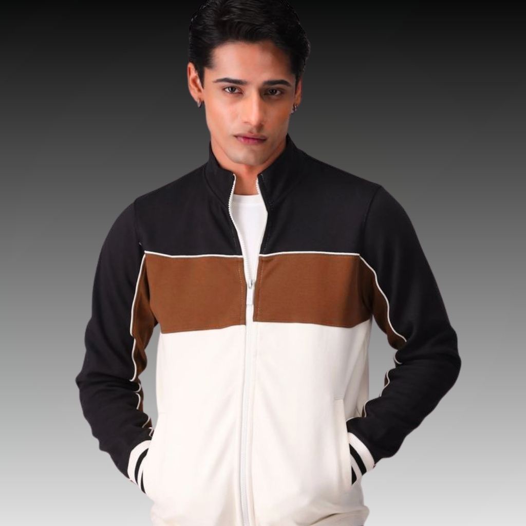 A man wearing a color-block zip-up jacket in black, brown, and white, posing with hands in pockets against a dark-to-light gradient background.