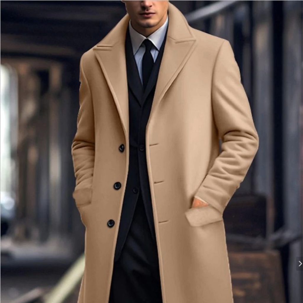 Person wearing a tan overcoat over a black suit with a white shirt and black tie, standing outdoors with hands in pockets.