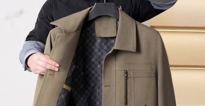 A person holding up an olive-brown jacket, showing the coat’s interior lining and a zippered chest pocket.