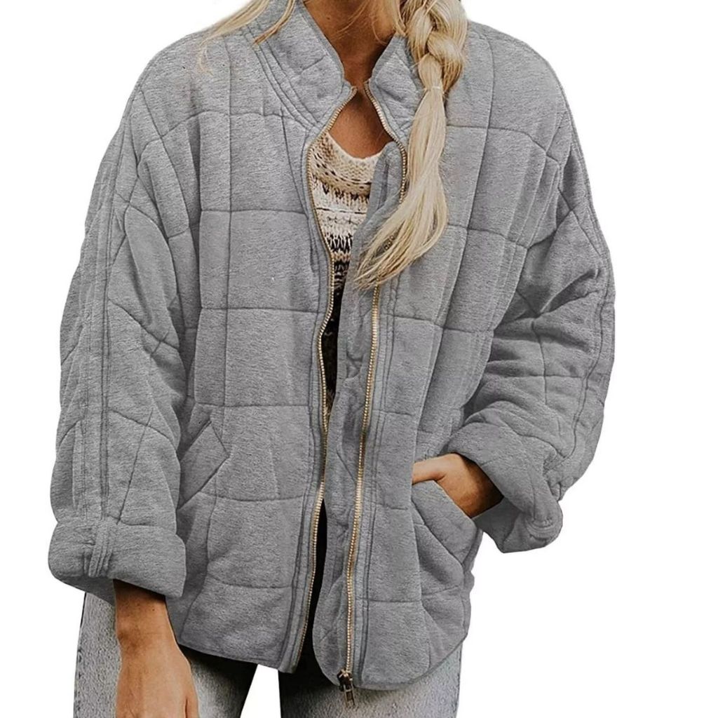 A cropped, oversized gray quilted jacket with a front zipper, rolled cuffs, and a relaxed fit worn by a woman with a long braided ponytail.
