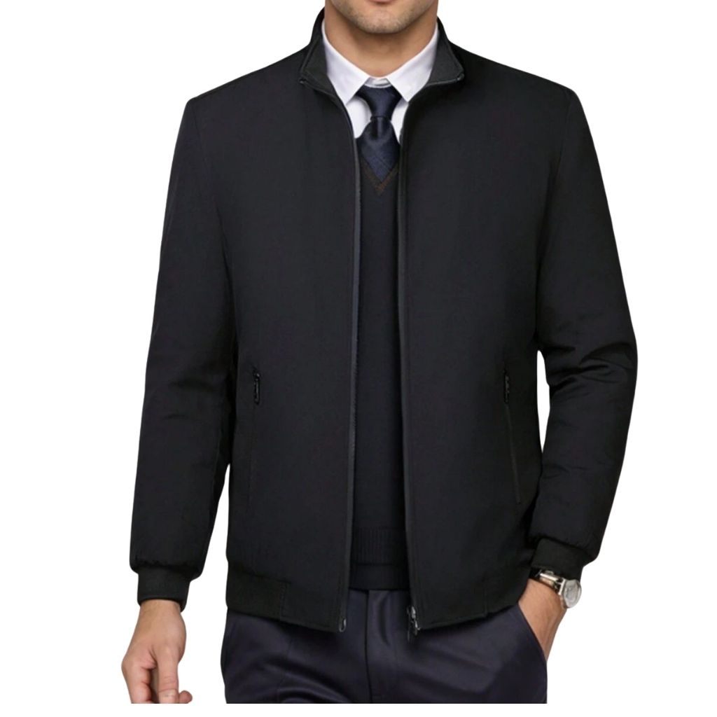A man wearing a sleek black office jacket over a white shirt and navy sweater, with a zip-up front and ribbed cuffs.