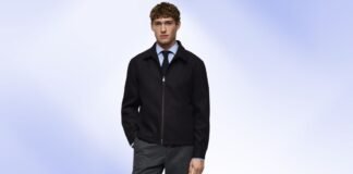 Office Jacket: The Best Blend of Style and Comfort Young man wearing a black zip-front jacket over a light blue shirt and dark tie, standing against a soft blue background.