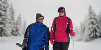 Ski Jacket: Winter Protection, Warmth, & Performance "Two skiers standing in a snowy, forested landscape. One wears a bright blue and black ski jacket with a helmet and goggles; the other wears a pink and black ski jacket with a beanie and goggles, holding ski poles.