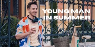 Summer Overshirt Jacket: Lightweight Style for Warm Days Now A young man stands outdoors near a decorative iron fence, smiling while holding a cup. He has a colorful shirt over a light t-shirt, wears headphones around his neck, and a bicycle with a basket and a tote bag is nearby.