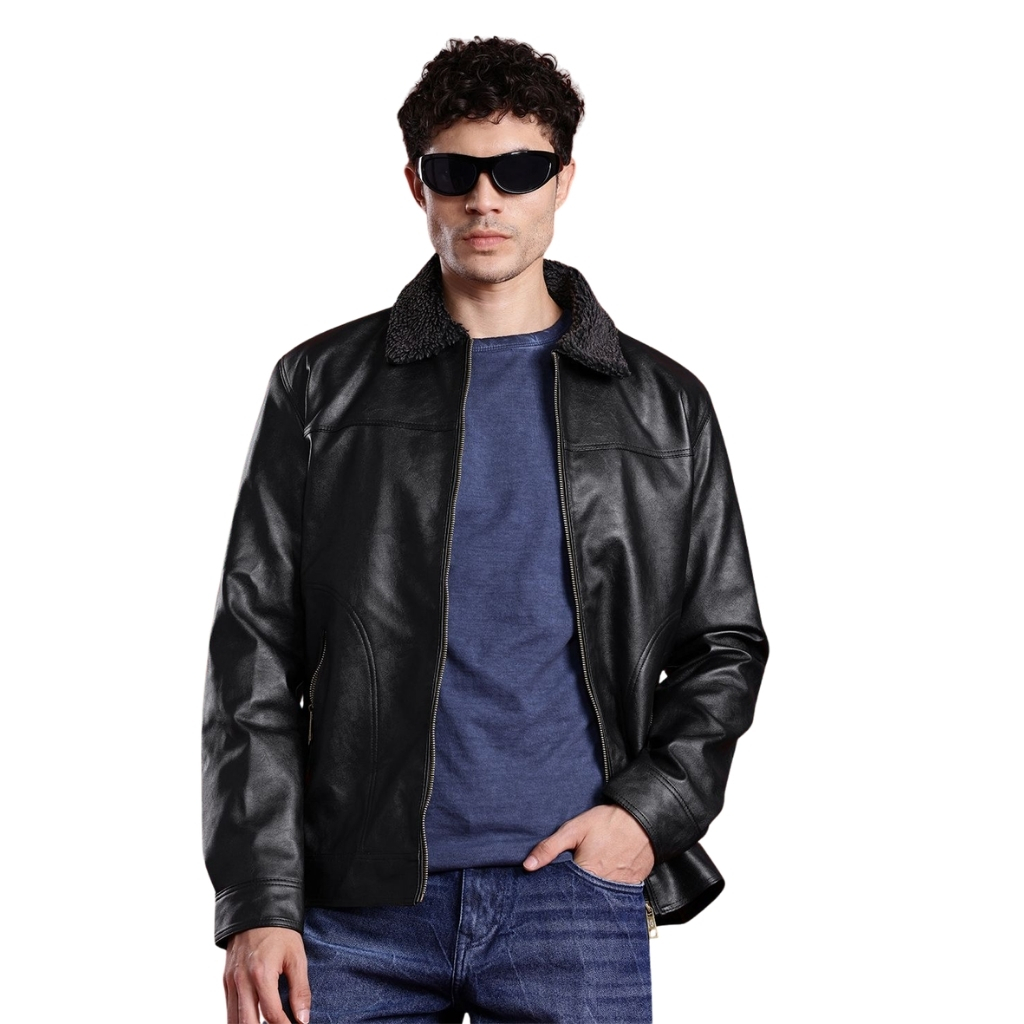 A man wearing a black leather jacket with a shearling collar, a blue T-shirt, and jeans. He has dark sunglasses and curly hair, with one hand in his pocket, standing against a white background. The jacket is zipped up halfway, highlighting the leather texture.