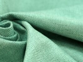 Brushed Grade C Cashmere Fabric Close-up of light green brushed cashmere fabric with a twill weave, folded into a swirl on the left.