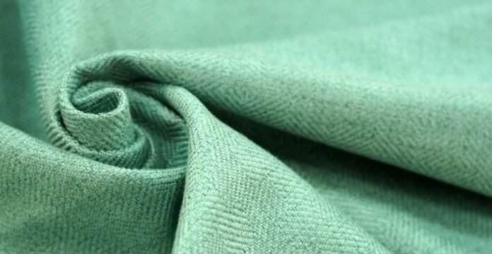 Brushed Grade C Cashmere Fabric Close-up of light green brushed cashmere fabric with a twill weave, folded into a swirl on the left.