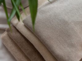 Brushed Pure Cashmere Fabric Guide Close-up of a stack of brushed cashmere fabrics in beige and brown tones, folded neatly on a white surface with blurred green plant leaves in the corner.