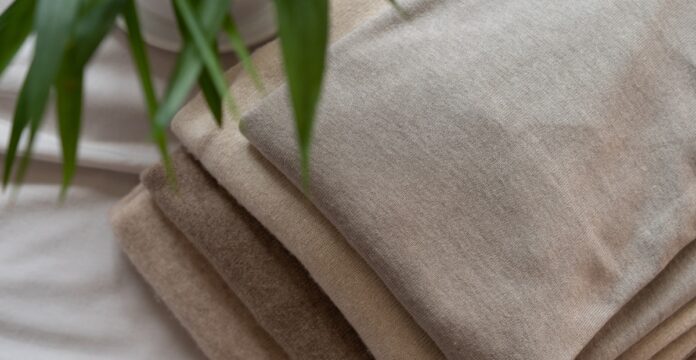 Brushed Pure Cashmere Fabric Guide Close-up of a stack of brushed cashmere fabrics in beige and brown tones, folded neatly on a white surface with blurred green plant leaves in the corner.