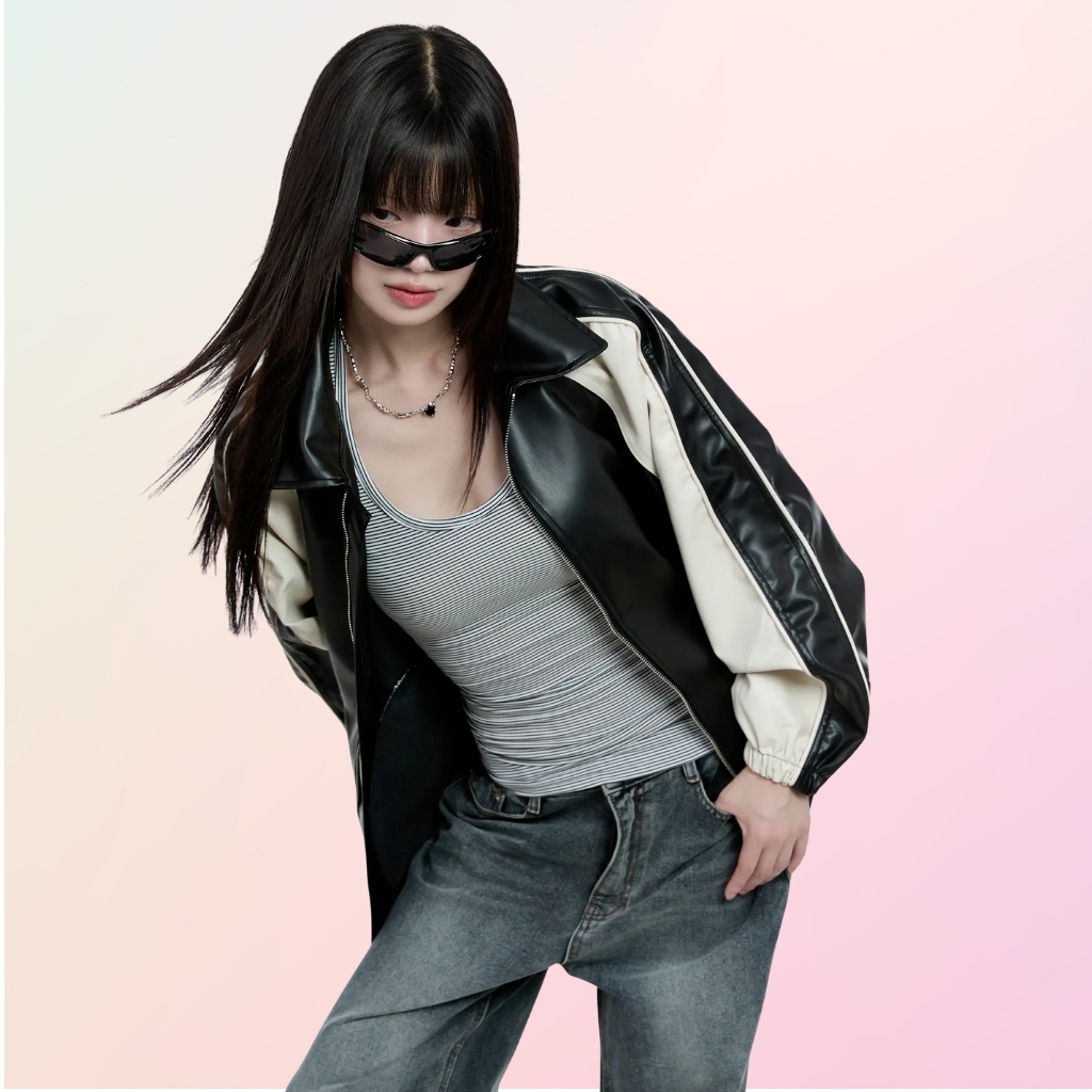 Two-Tone Leather Jacket for Bold Modern Everyday Street Style 7 A stylish young woman poses in a black-and-white leather jacket, striped tank top, and faded jeans, wearing dark sunglasses against a soft pink-to-white gradient background.