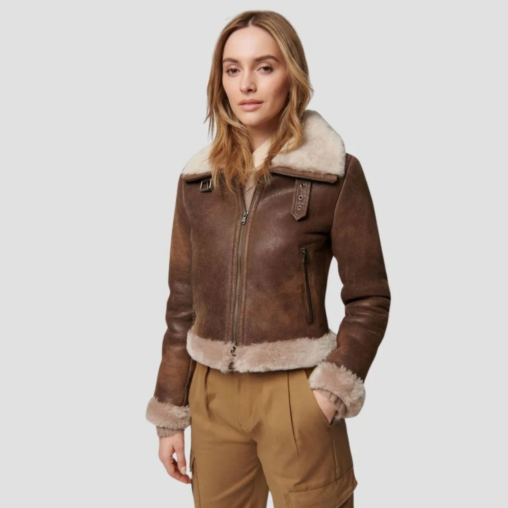 5 leather jacket for women Confidence & Style 8 A woman stands against a light gray background wearing a brown shearling leather aviator jacket with a cream shearling lining. The jacket has a zip front, zippered pockets, and rolled cuffs, paired with tan cargo-style pants.