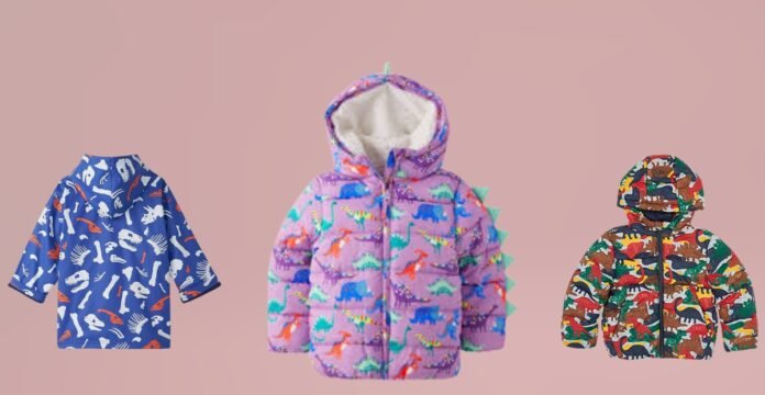 Three kids’ jackets displayed against a pink background: a blue jacket with white dinosaur bones and orange dinosaur silhouettes on the left, a lavender-purple puffer jacket with colorful dinosaurs and mint-green dinosaur spikes along the hood in the center, and a multicolored dinosaur camouflage puffer jacket on the right. Caption: