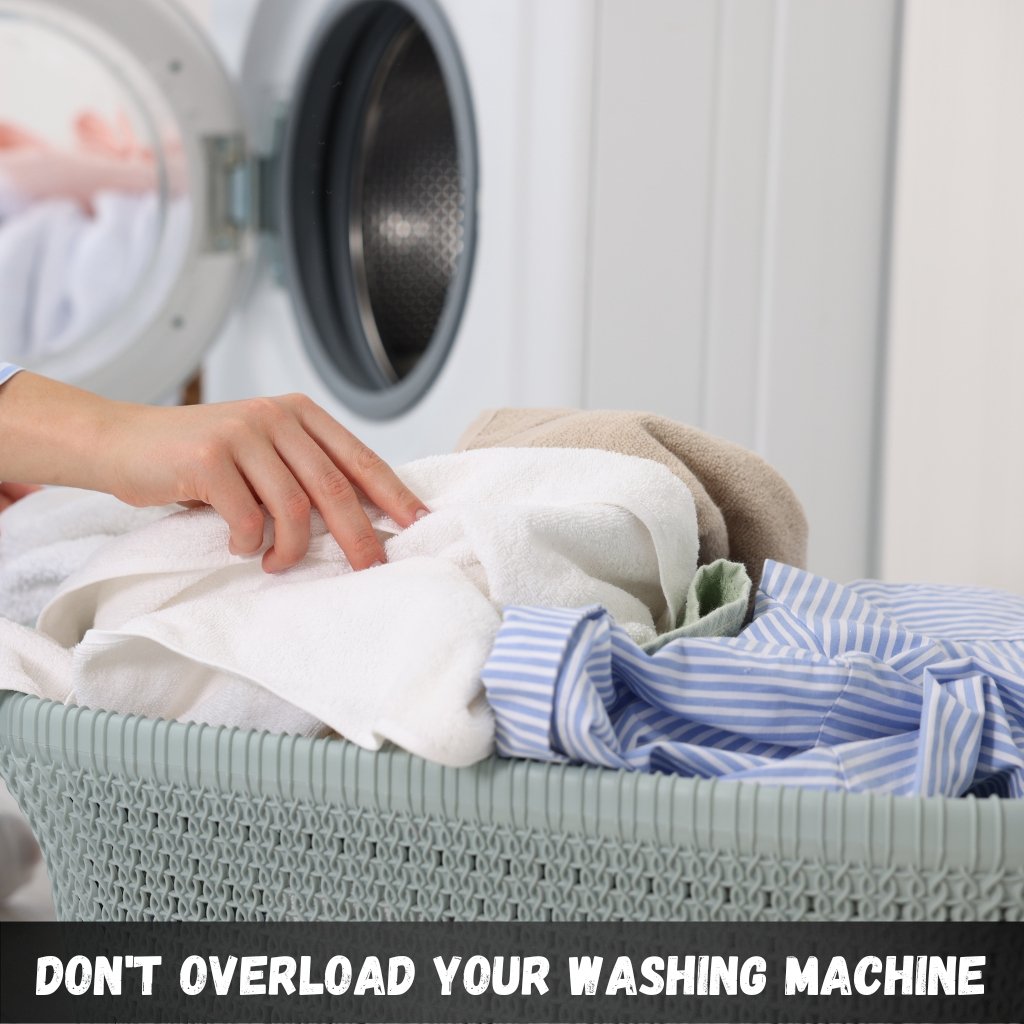 A hand places clothes into a laundry basket in front of a washing machine with its door slightly open.