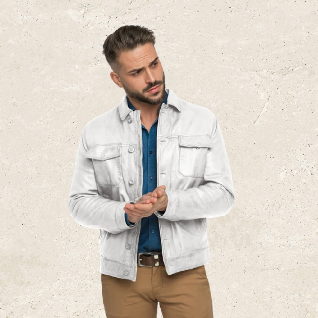 Premium Shirt Style Leather Jacket for Casual and Formal Looks 6 A stylish man with a beard wearing a light gray leather jacket over a blue denim shirt and khaki pants, standing against a textured off-white wall, looking to the left with his hands clasped in front of him.