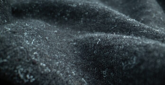 Felted Pure Cashmere Fabric Close-up of dark gray felted cashmere fabric with small white fibers or lint attached; fabric is draped with soft, fuzzy texture.