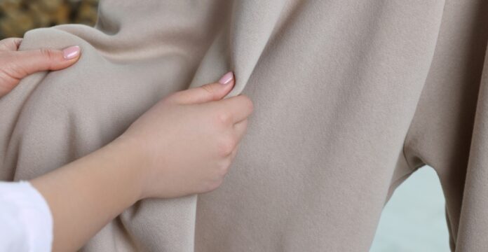 Heavyweight Grade C Cashmere Fabric Alt text: Close-up of a woman's hand holding a beige cashmere garment, showing the fabric’s texture and drape. Caption: Beige heavyweight cashmere fabric, held to showcase its texture and drape.