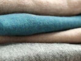 Heavyweight Pure Cashmere Fabric Close-up of a neat stack of folded heavyweight cashmere sweaters in beige, teal, beige, and gray, with prominent knit textures.