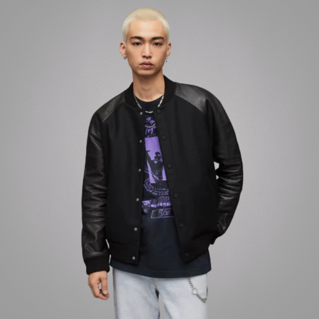 "A stylish varsity leather jacket paired with jeans and sneakers, worn casually by a person walking down a city street on a sunny day.