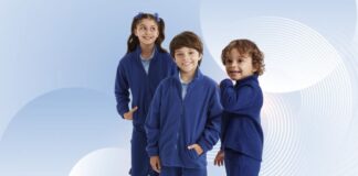 Kids Fleece Jacket for Boys & Girls | Soft Winter Wear Three children wearing matching blue fleece jackets and pants, standing side by side against a blue and white abstract background; a girl with pigtails and blue bows on the left, a smiling boy in the middle, and a younger boy with curly hair on the right.