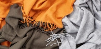 Knitted Grade B Cashmere Fabric: Affordable Everyday Luxury A close-up of a tangled pile of three scarves in orange, olive green, and light grey, showing woven textures and fringed edges.