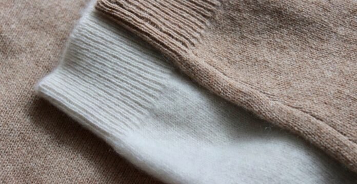 Knitted Grade C Cashmere Fabric Close-up of a beige and white knitted cashmere sweater, showing the beige main fabric with a white ribbed cuff.