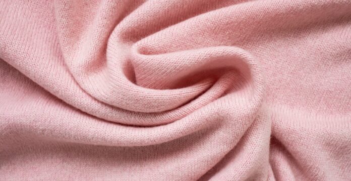 Lightweight Grade C Cashmere Fabric Close-up of a soft pink knitted cashmere fabric arranged in a twisting spiral, showing the fine knit texture and gentle folds.
