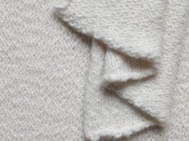 Lightweight Recycled Cashmere Fabric A close-up view of a cream-colored knitted fabric with a wavy, folded edge, showing the textured knit pattern.