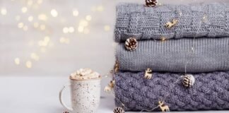 Winter Lock Fabric: The Secret Behind Ultra-Warm Winter Wear Alt text: A cozy winter scene showing a white speckled mug filled with marshmallows beside a stack of folded knit sweaters in gray and charcoal tones, with small decorative pinecones and string lights in the background.Winter Lock Fabric: