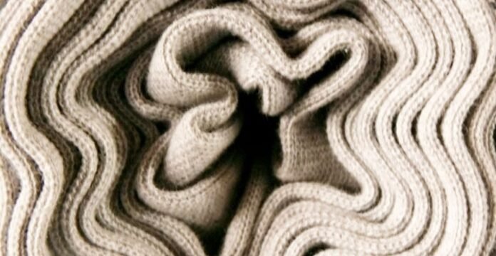 Alt text: Close-up of a folded, cream-colored knit fabric with thick, wavy ridges creating a plush, textured appearance. What Is Thermal Core Fabric for Winter Wear?