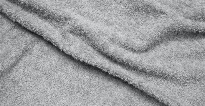 Alt text: Close-up of a gray plush towel with a soft, fluffy texture and gentle folds casting shadows. Polar Warm Weave Fabric Explained: