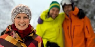 Snow-Resistant Fabric Explained: Stay Dry, Warm & Protected Alt text: Group of three friends standing outdoors in a snowy landscape. The woman in the foreground wears a colorful plaid jacket and knit hat, smiling at the camera. Behind her, two men wearing bright yellow and orange winter jackets with hats and goggles smile as well; the background shows snowy trees and a wintry scene. Snow-Resistant Fabric Explained: