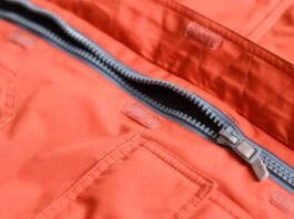 Close-up of an orange winter coat with a partially unzipped gray-lined zipper; visible pockets and Velcro closures along the fabric.Storm Warm Insulation Fabric: