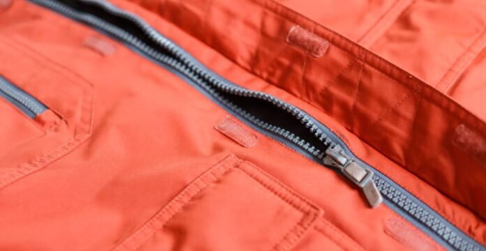 Close-up of an orange winter coat with a partially unzipped gray-lined zipper; visible pockets and Velcro closures along the fabric.Storm Warm Insulation Fabric: