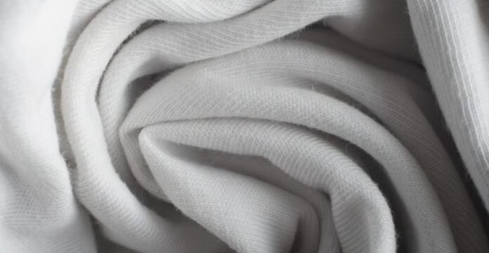 Alt text: Close-up of white woven fabric in soft folds, showing fine ribbed texture and diffused shadows. Frost Flex Stretch Thermal Fabric: