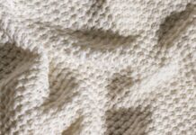 Arctic Hug Comfort Weave: The Ultimate Winter Warmth Fabric Alt text: Close-up of a cream-colored knit blanket with a dense, square pattern creating a three-dimensional texture; the blanket is draped and folded, casting soft shadows. Arctic Hug Comfort Weave: