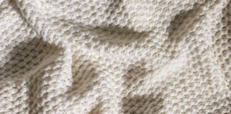 Arctic Hug Comfort Weave: The Ultimate Winter Warmth Fabric Alt text: Close-up of a cream-colored knit blanket with a dense, square pattern creating a three-dimensional texture; the blanket is draped and folded, casting soft shadows. Arctic Hug Comfort Weave: