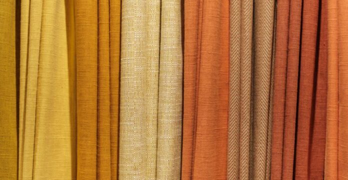 Alt text: Close-up of vertical fabric drapes in a gradient from light yellow to dark orange, showing a mix of smooth and textured surfaces. Warm Aura Fabric Explained: