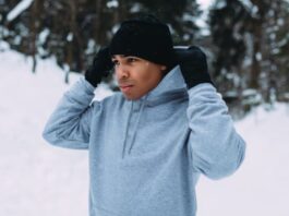 Snow Defense Performance Knit: Stay Warm & Active Outdoors A man in a black beanie and gloves adjusts a gray hoodie in a snowy outdoor setting with snow-covered trees in the background.Snow Defense Performance Knit: