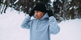 Snow Defense Performance Knit: Stay Warm & Active Outdoors A man in a black beanie and gloves adjusts a gray hoodie in a snowy outdoor setting with snow-covered trees in the background.Snow Defense Performance Knit: