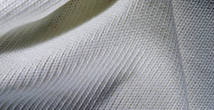 Alt text: Close-up of a creamy white knit fabric with a ribbed pattern, showing folds and soft shadows that highlight texture. What Is Heat Retain Pro Weave Fabric?
