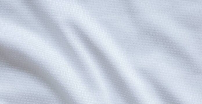 Alt text: Close-up of white textured fabric with subtle weave, featuring soft folds and gentle shadows. Ice Glow Comfort Weave Fabric: