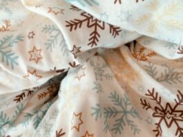 Close-up of wrinkled white fabric with a repeating pattern of brown and blue snowflakes and gold stars.Winter Crown Insul-Fabric Guide:
