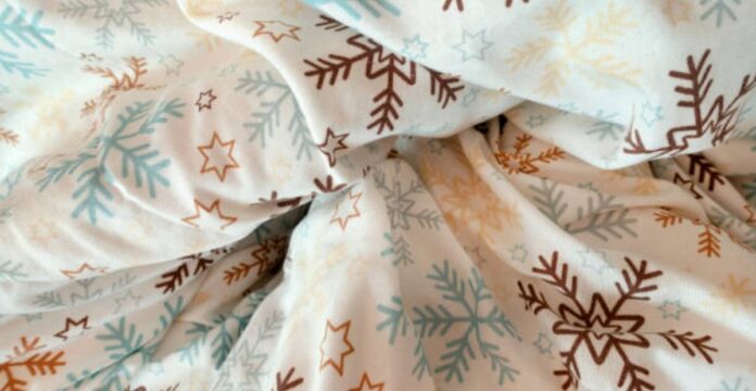 Close-up of wrinkled white fabric with a repeating pattern of brown and blue snowflakes and gold stars.Winter Crown Insul-Fabric Guide: