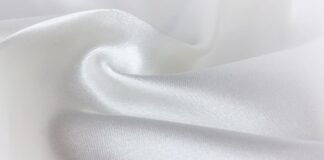 Snow Aura Premium Shield Fabric: Features, Benefits & Uses Close-up of soft, white satin fabric. The material is draped and folded, with gentle movement and a subtle sheen from diffused lighting. Snow Aura Premium Shield Fabric: