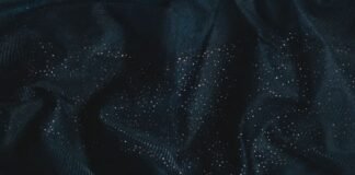 Winter Glow Supreme Fabric: High-Performance Winter Textile A close-up of dark blue sheer fabric with numerous small glittering silver speckles, gathered and folded to show texture and depth. Winter Glow Supreme Fabric: