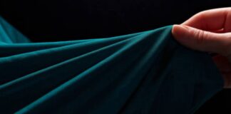 Ultra Motion Stretch Fabric: Performance, Durability & Style A close-up of teal fabric being held and draped by a hand, with soft folds and a dark background. Ultra Motion Stretch Fabric: