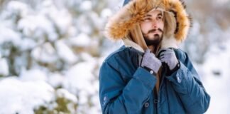 Extreme Cold Protection Winter Coat: Best Snowstorm Choice "Man outdoors in a snowy landscape wearing a blue winter parka with a fur-lined hood, looking off to the side and adjusting his scarf." Ultra-Warm Thermal Winter Coat: